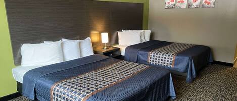 A hotel room with two beds, a headboard, a nightstand, a lamp, and a wall with four framed pictures.