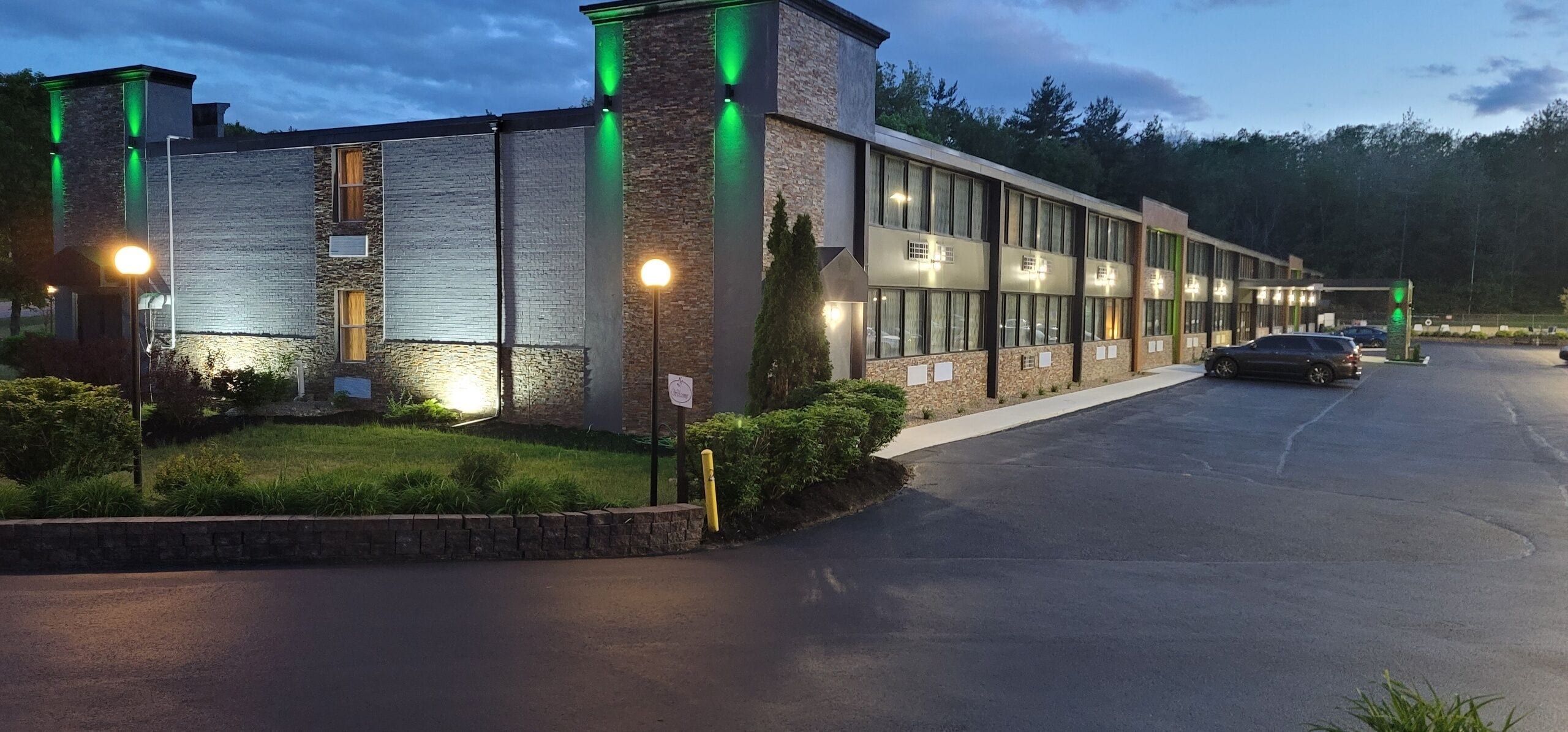 A modern building with a parking lot and a green-lit entrance.