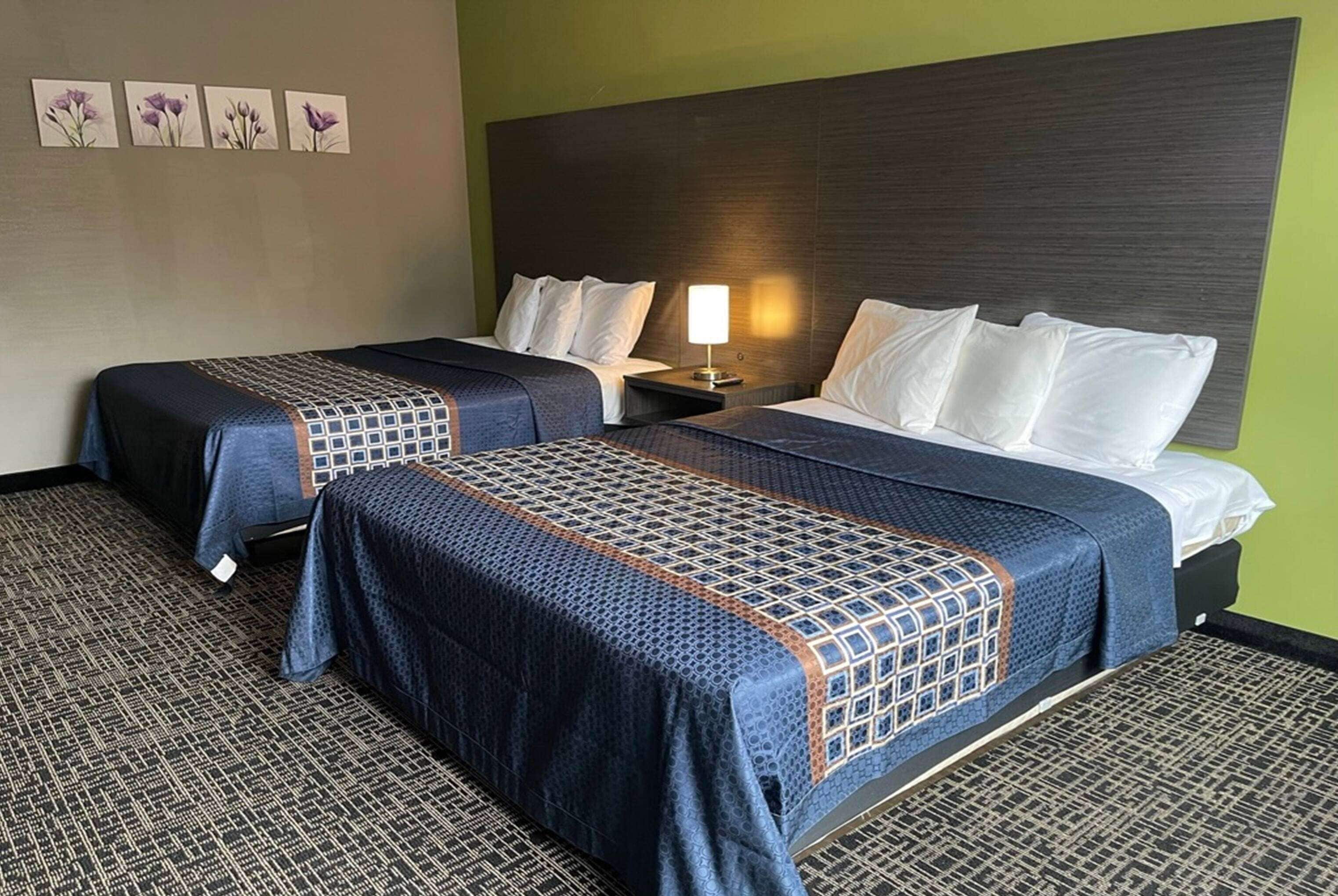 Ein Hotelzimmer mit zwei Betten, einem Nachttisch mit Lampe und einer Wand mit floralem Kunstwerk.