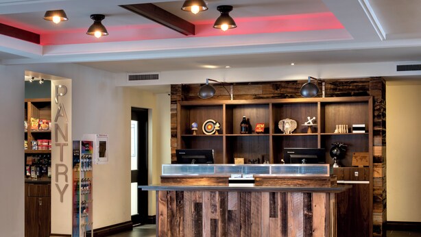A modern lobby with a wooden reception desk, a vending machine, and a 'PANTRY' sign. - The Crossroads Hotel, Newburgh (Newburgh)