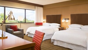 A hotel room with two beds, a desk, a chair, a lamp, and a window with a view of trees. - The Crossroads Hotel, Newburgh (Newburgh)