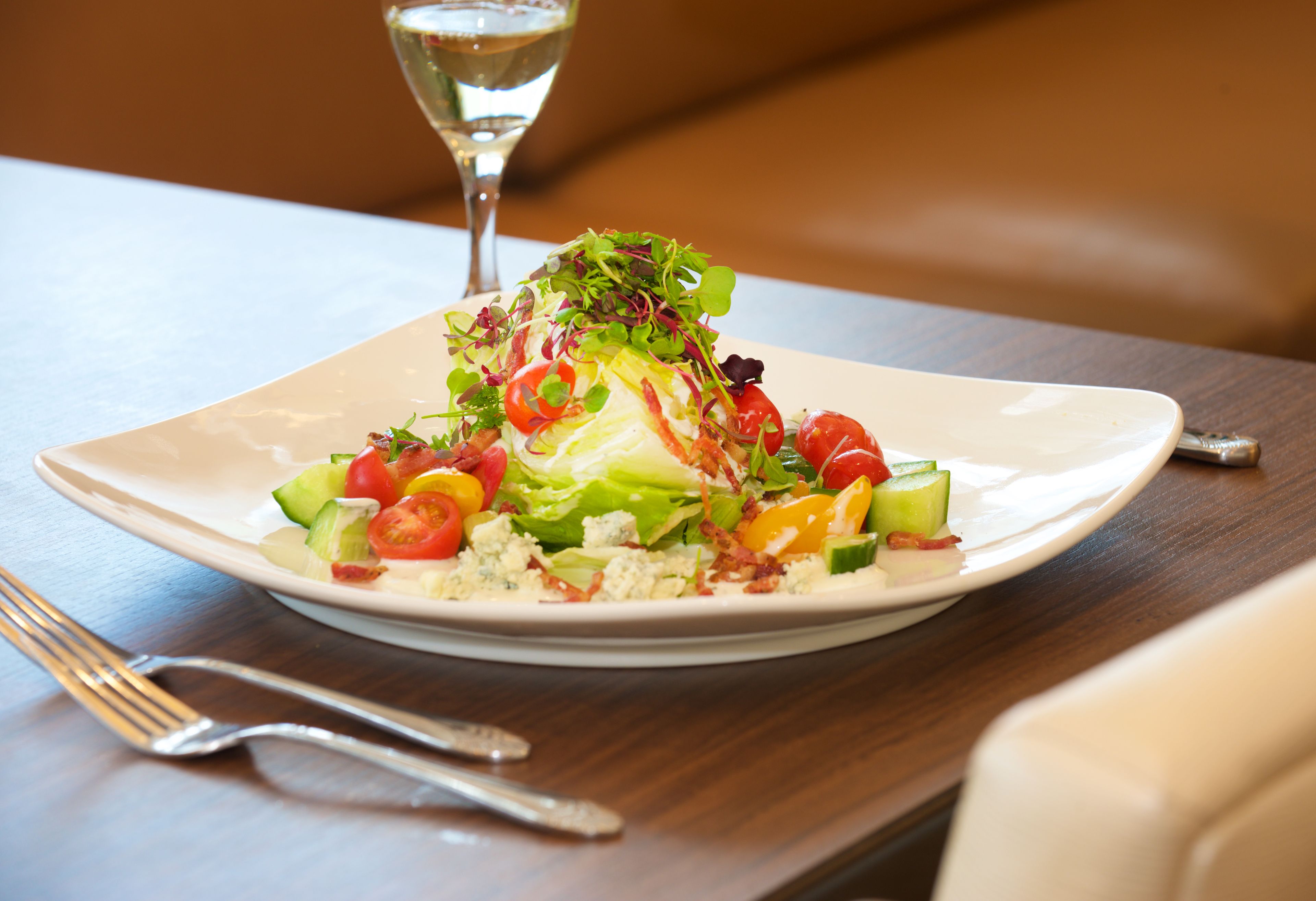 A square white plate with a salad on a wooden table.