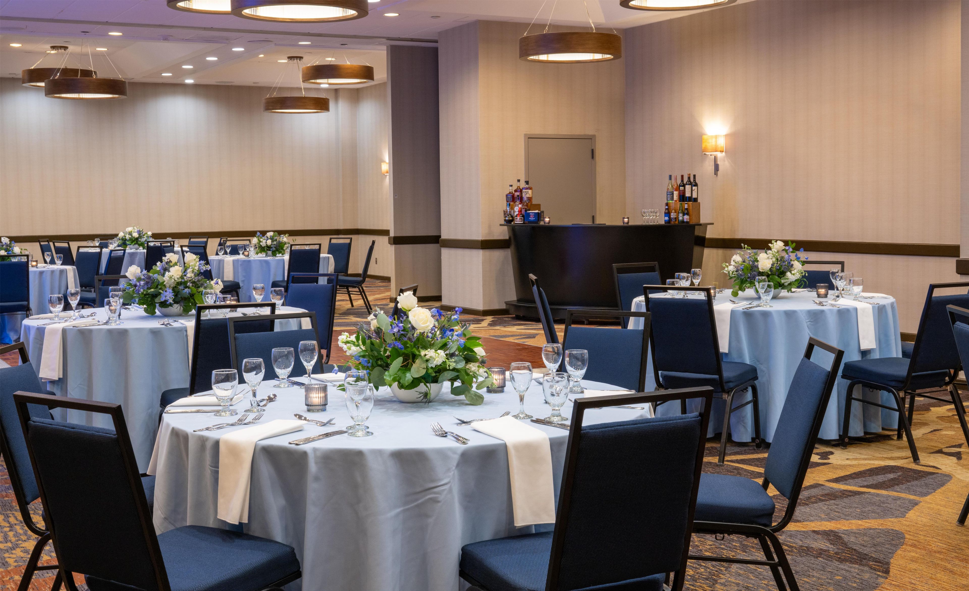 A banquet hall with round tables, chairs, and floral centerpieces.