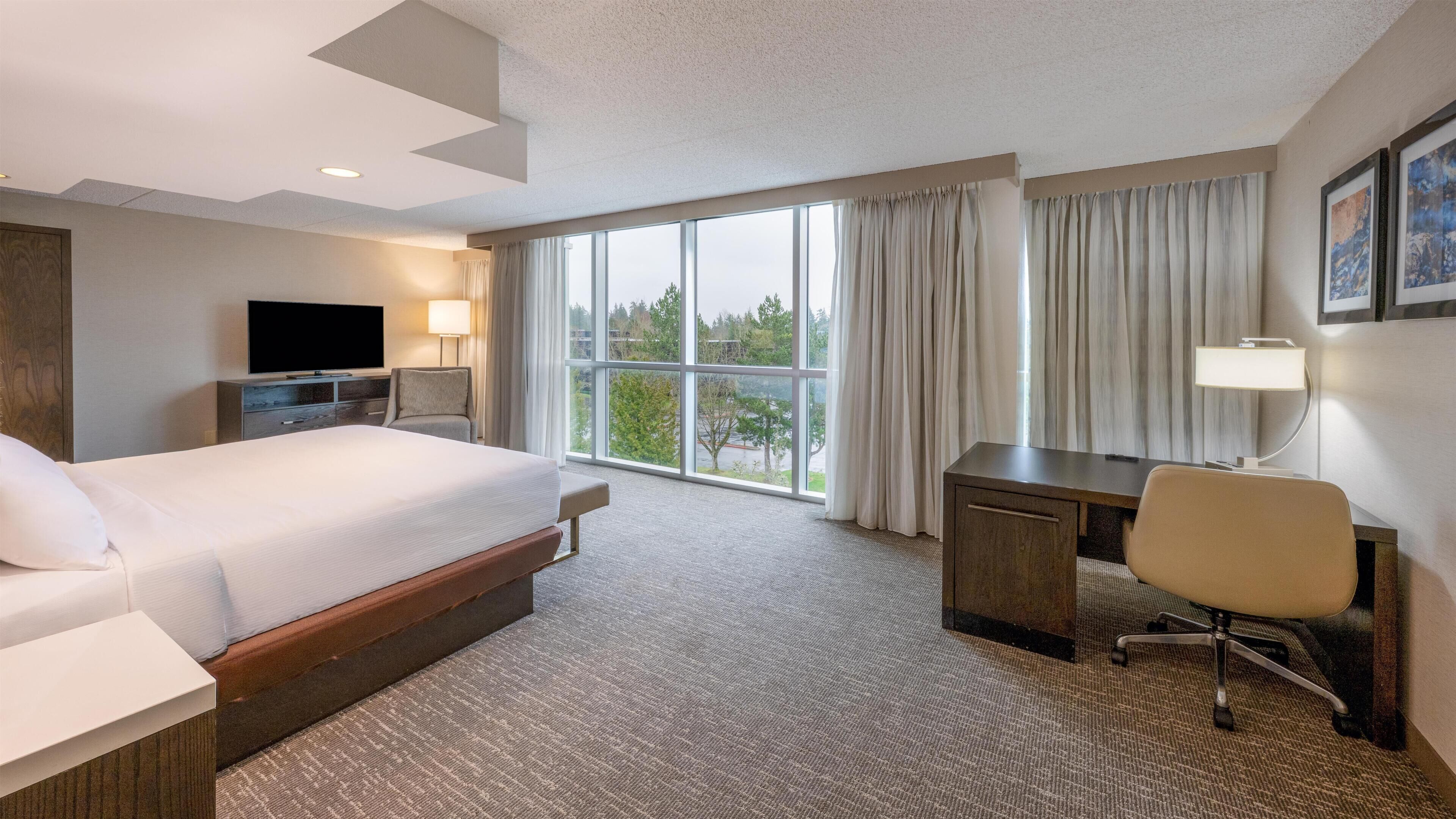 A hotel room with a large bed, a desk, a chair, a TV, and a window with curtains.