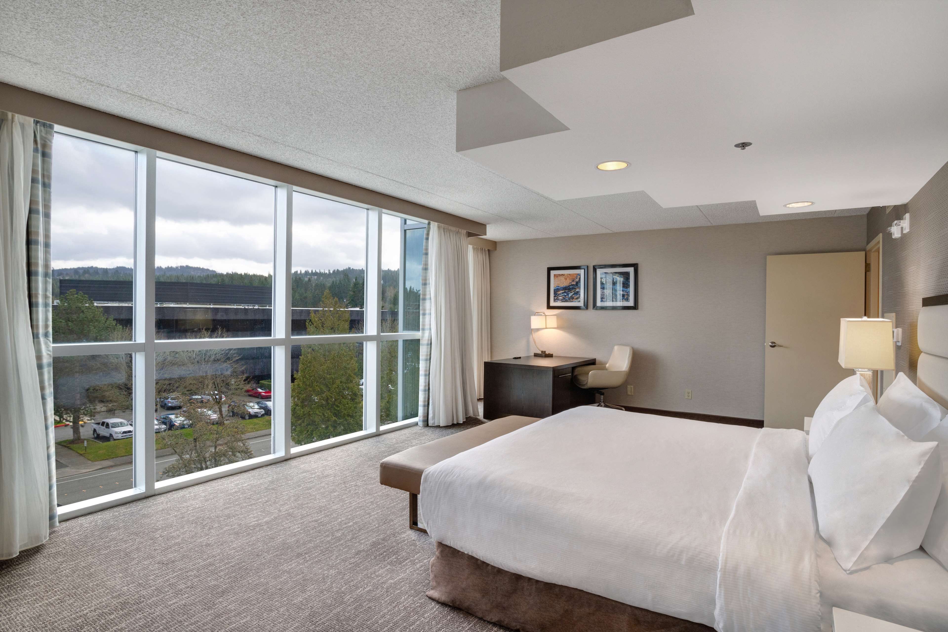 A hotel room with a large window, a bed, a desk, and a chair.