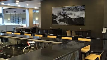 Zona de bar con una barra alargada, varios taburetes y un cuadro grande con una vista marina en la pared.