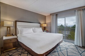 A hotel room with a large bed, two bedside tables with lamps, a view of the outdoors through a balcony. - Embassy Suites by Hilton Seattle Bellevue (Bellevue)