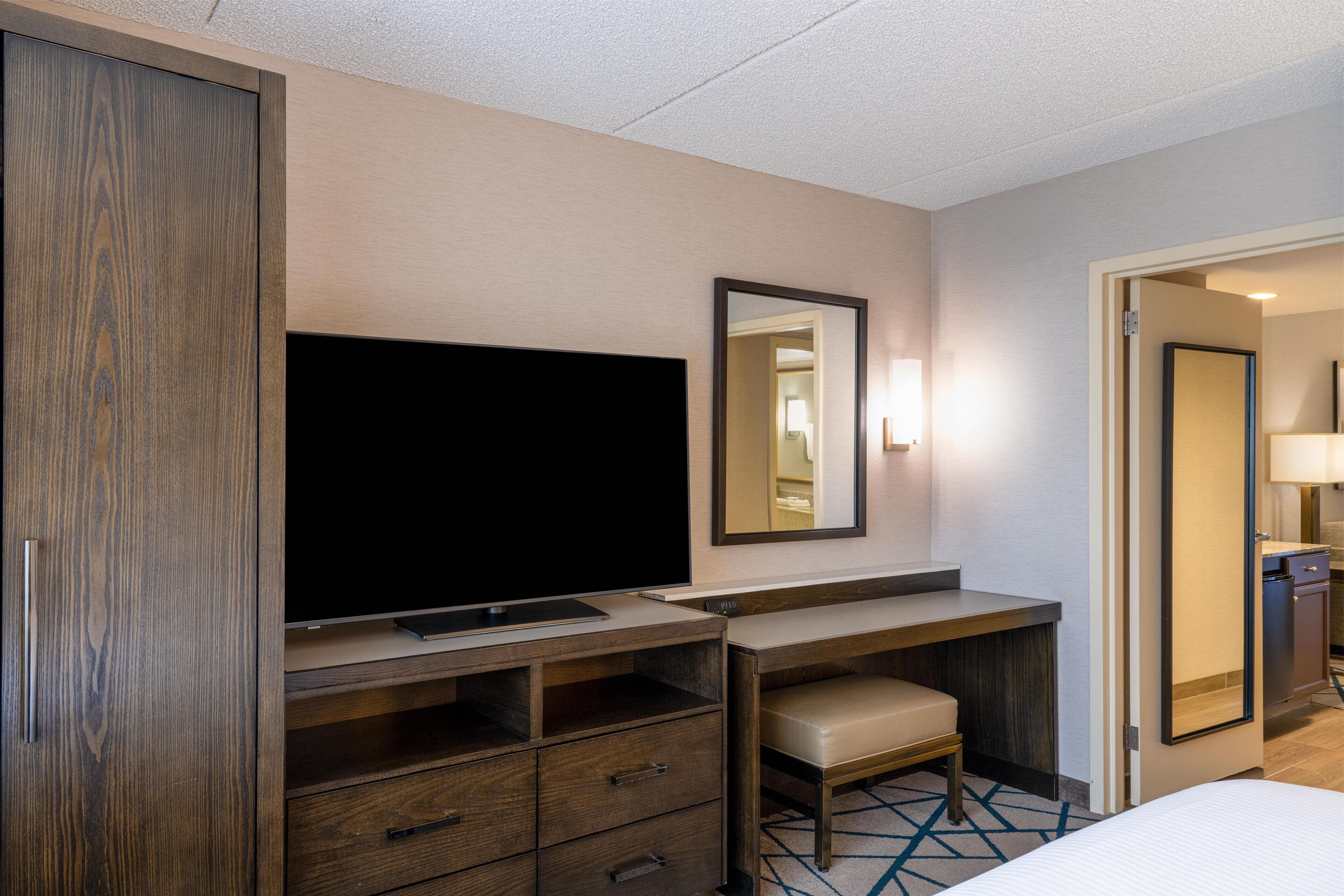 Hotelkamer met een flatscreen televisie, een bureau met stoel, een spiegel en een deur naar een badkamer.