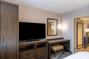 A hotel room with a flat-screen TV, a desk with a chair, a mirror, and a door leading to a bathroom. - Embassy Suites by Hilton Seattle Bellevue (Bellevue)