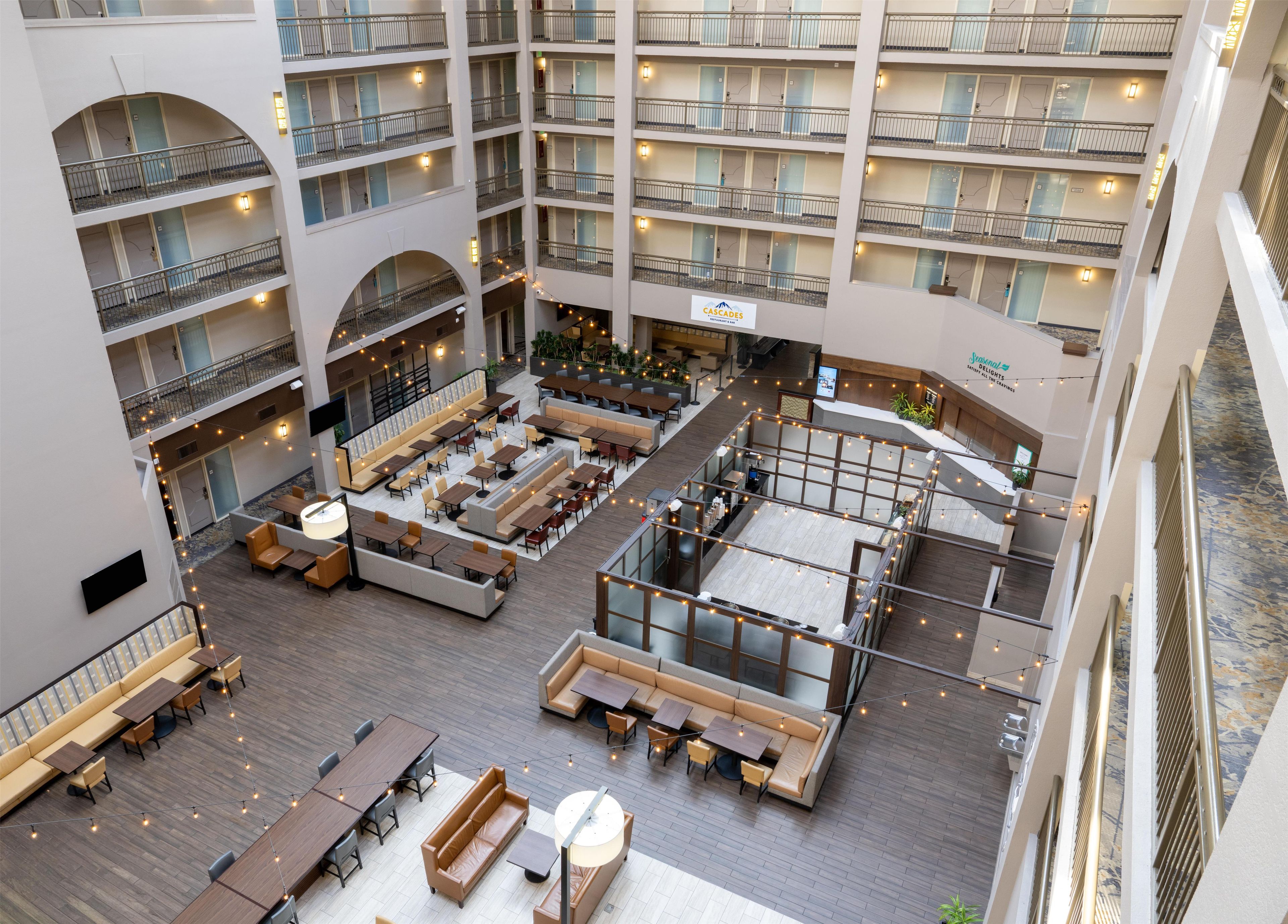 A multi-level hotel atrium with seating areas, a restaurant, and a sign for 'Cascades Delights.'
