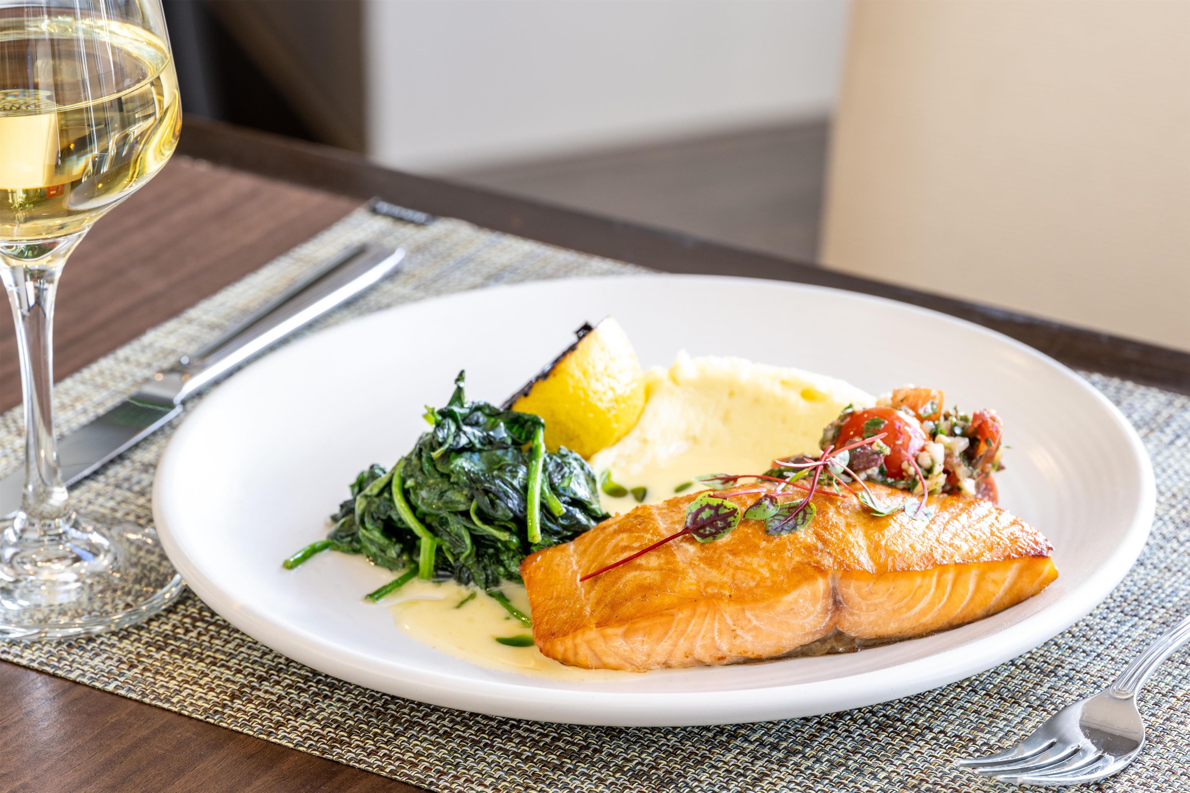 A plate of food with salmon, potatoes, and greens on a table.