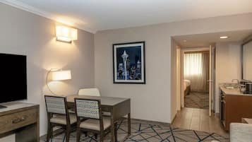 Habitación de hotel con comedor, televisor, una fotografía enmarco de un paisaje urbano y kitchenette.