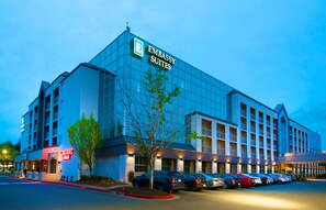 A modern building with a sign reading "Embassy Suites." It features multiple floors, a parking lot with several cars, and a tree in front. - Embassy Suites by Hilton Seattle Bellevue (Bellevue)