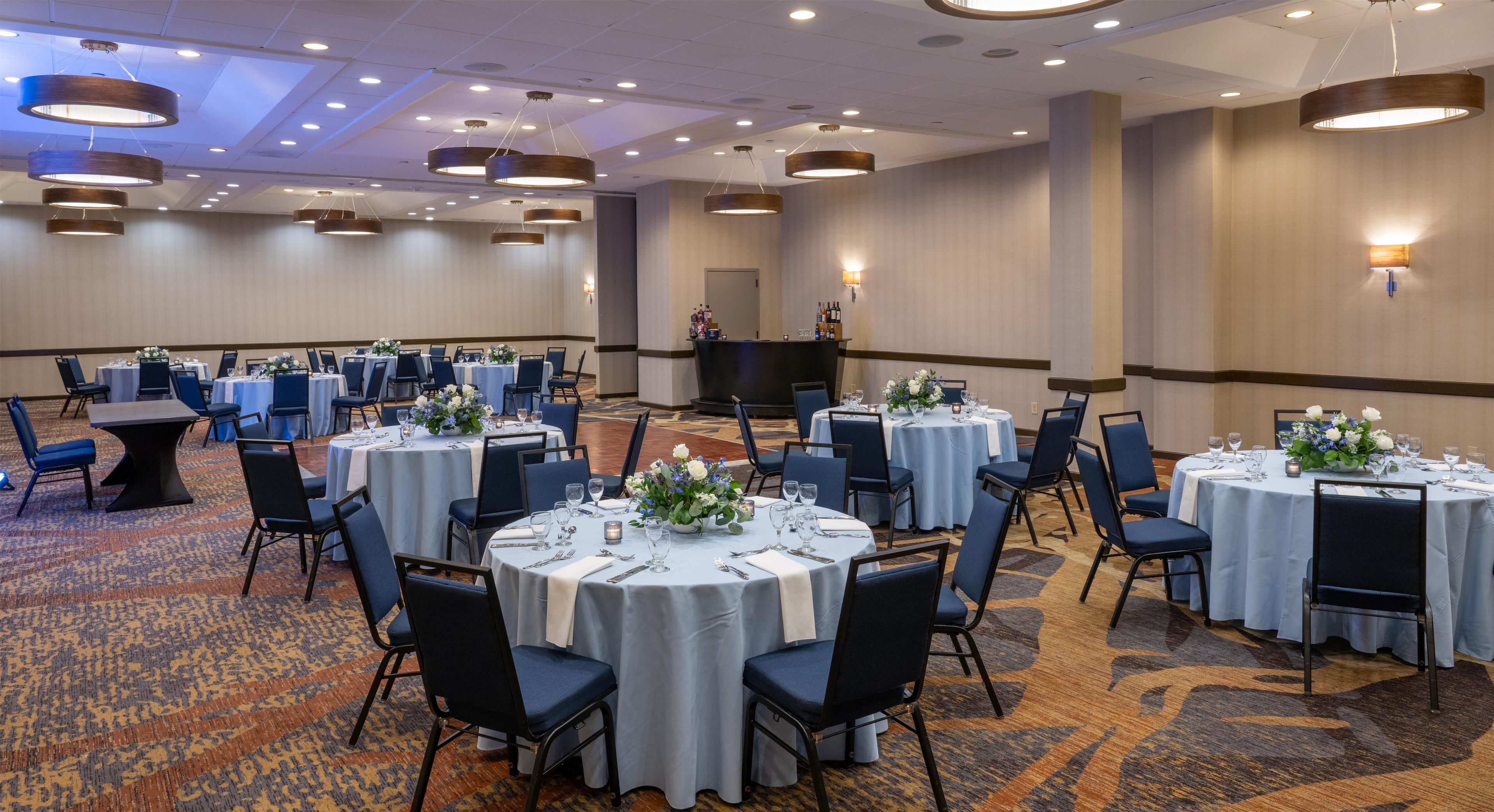 A conference room with multiple round tables, each set with chairs and tablecloths, and a stage area with a podium and seating.