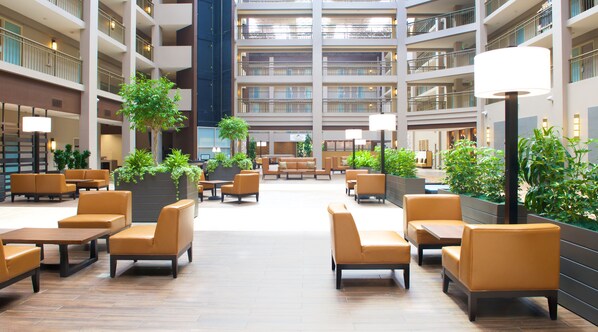 A spacious lobby with multiple seating areas, indoor plants, and a high ceiling with a central atrium. - Embassy Suites by Hilton Seattle Bellevue (Bellevue)