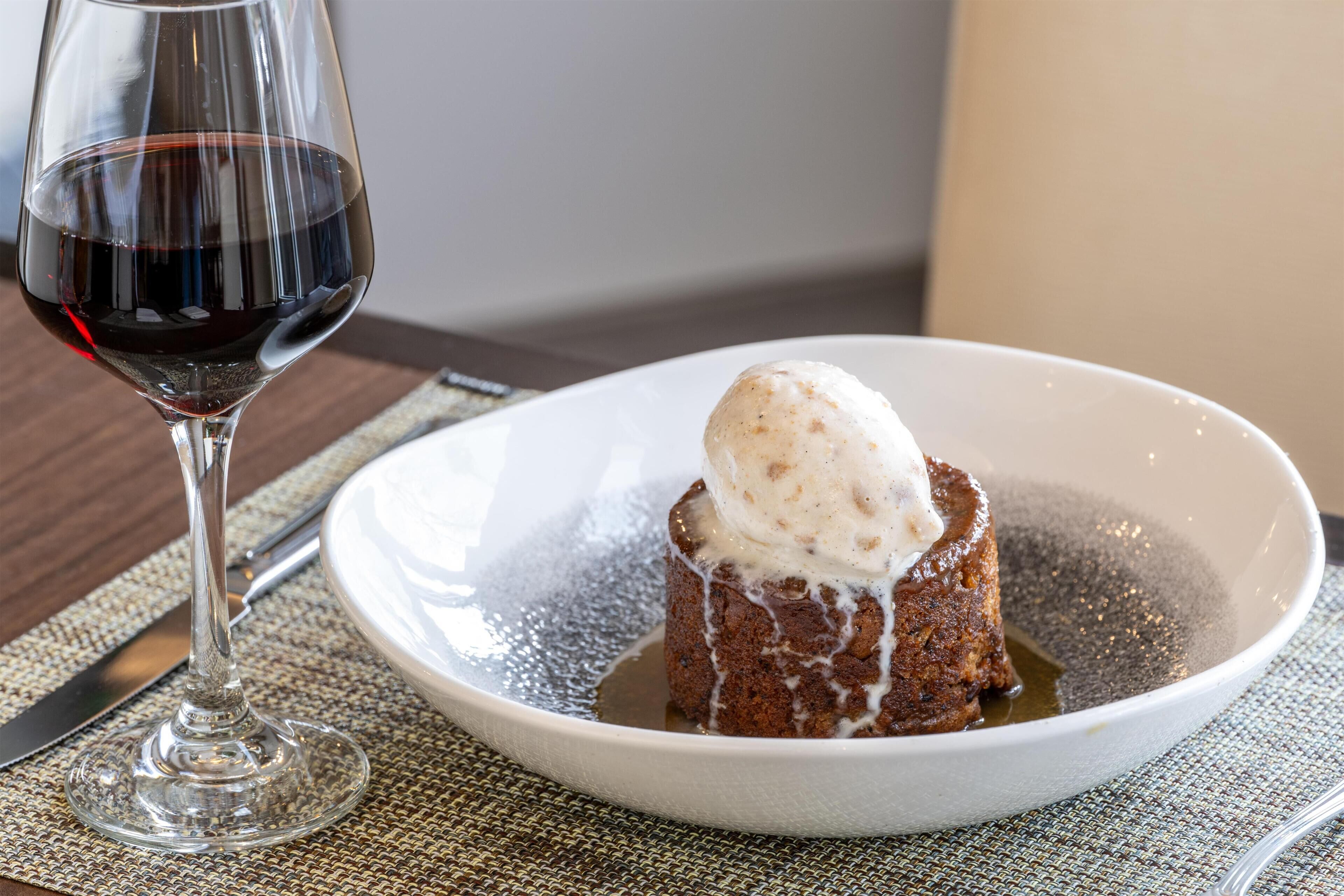 A dessert with ice cream on a plate, a wine glass, and a fork on a table.