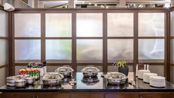 A buffet setup with food containers, plates, and utensils on a counter with a large window in the background.