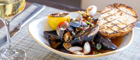 Un plato de mejillones con pan a la parrilla y una rodaja de limón sobre una mesa.
