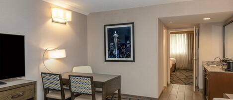 A hotel room with a dining area, a TV, a framed cityscape picture, and a kitchenette.
