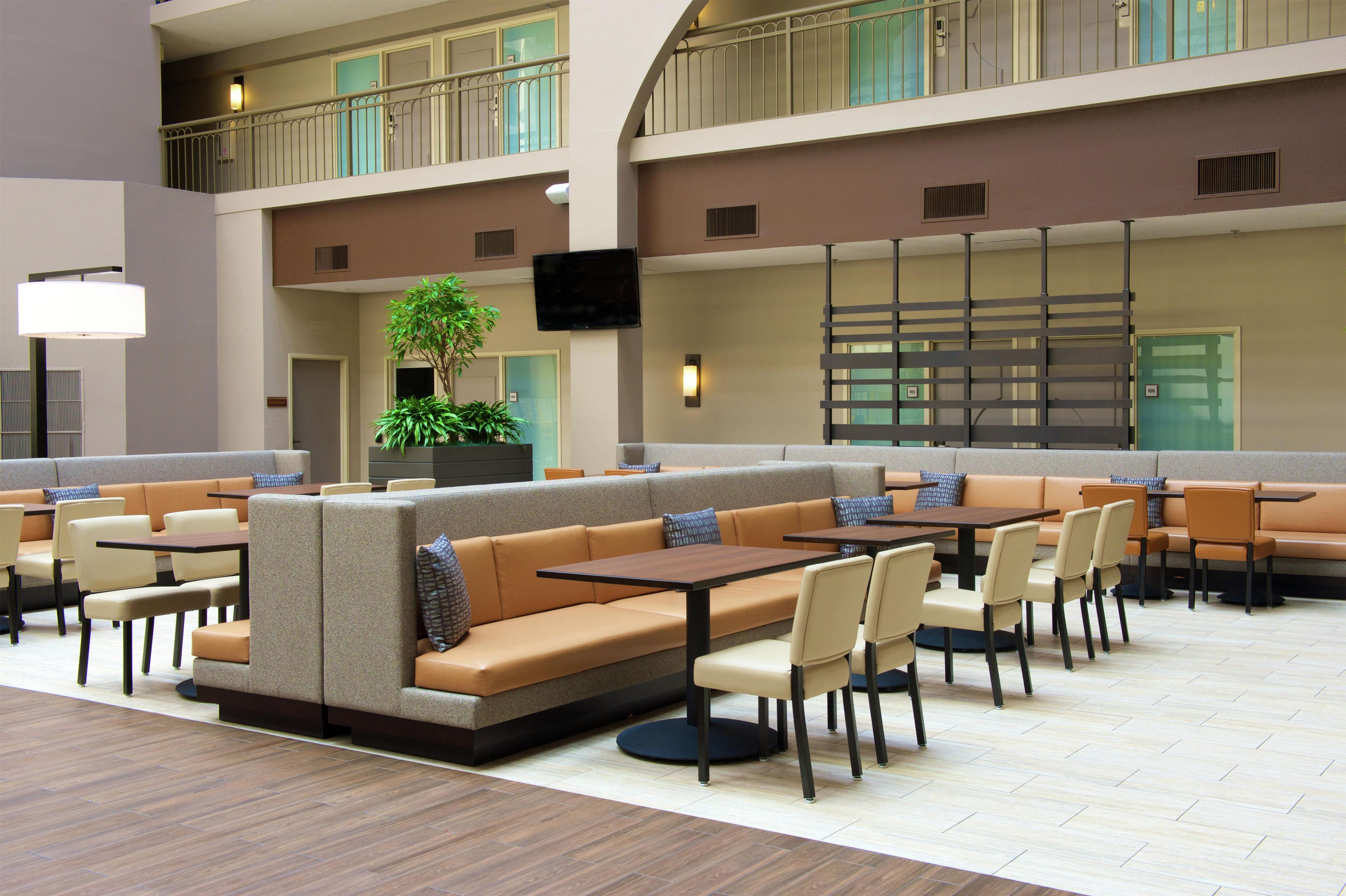 A spacious indoor seating area with multiple tables and cushioned seating, a large plant, and a flat-screen TV mounted on the wall.