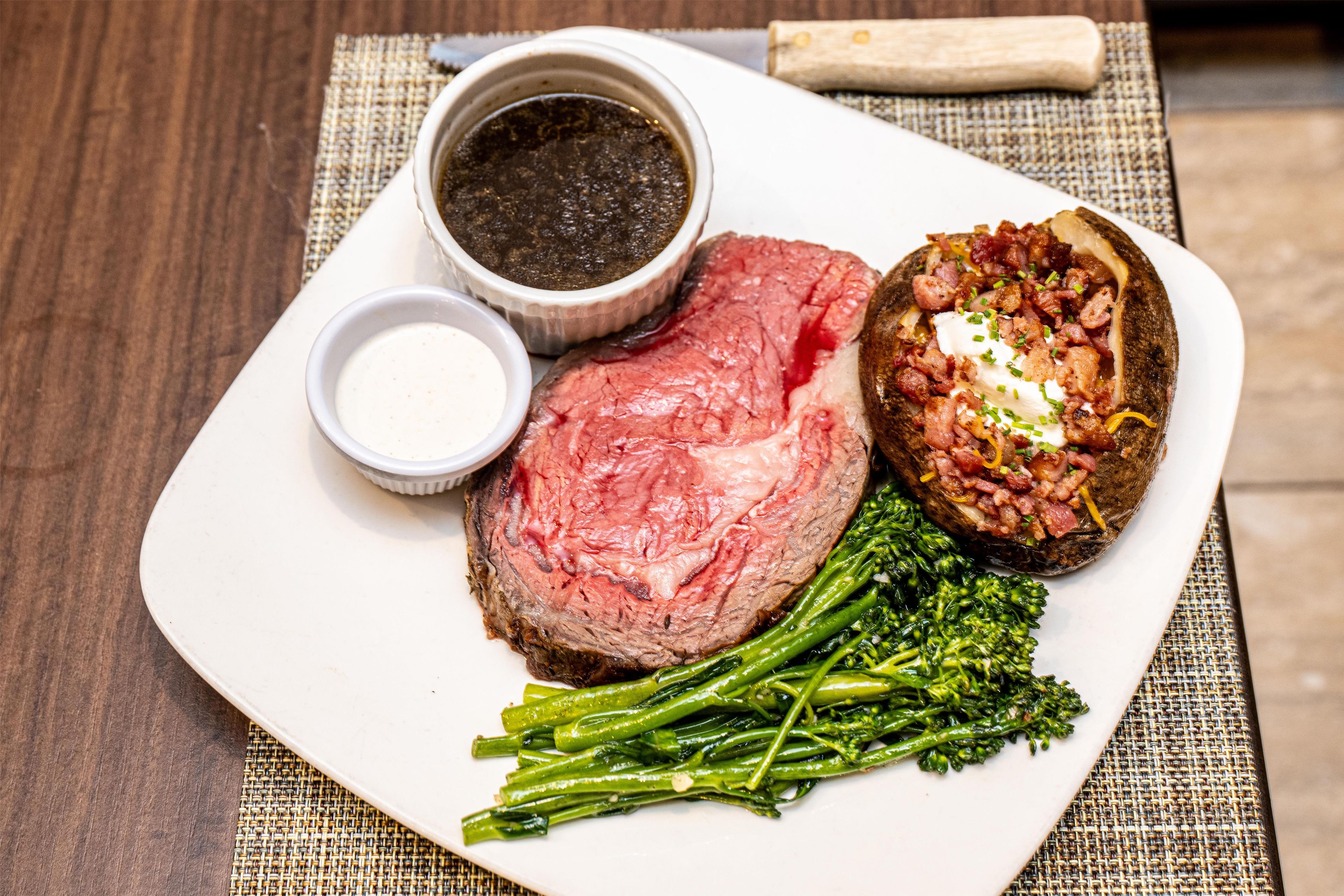 Une assiette contenant un steak, une pomme de terre au four et des haricots verts, accompagnée de deux petits ramequins de condiments.