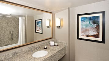A bathroom with a granite countertop, a white sink, a large mirror, and framed artwork on the wall.