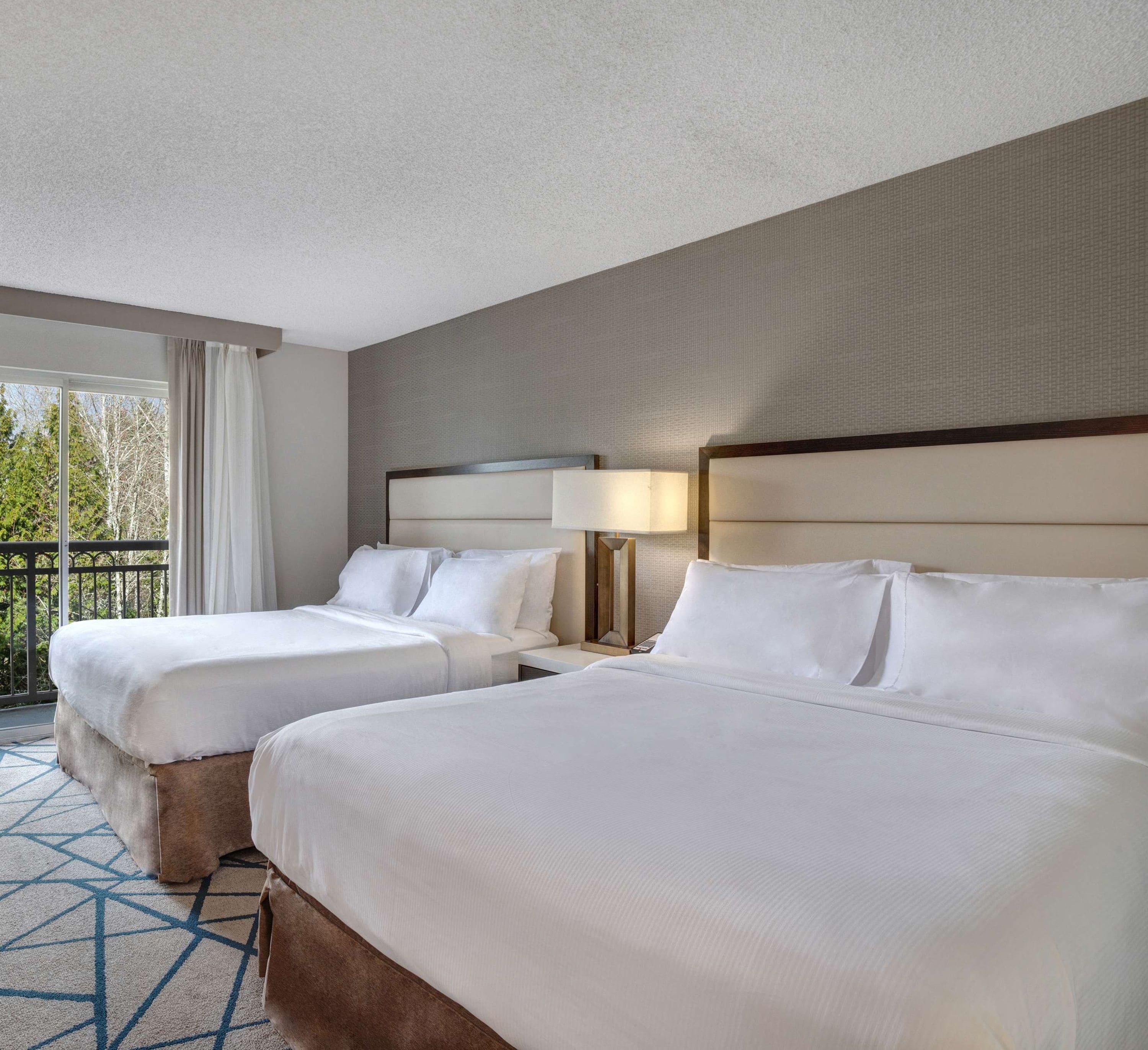 A hotel room with two beds, a balcony, and a view of trees.