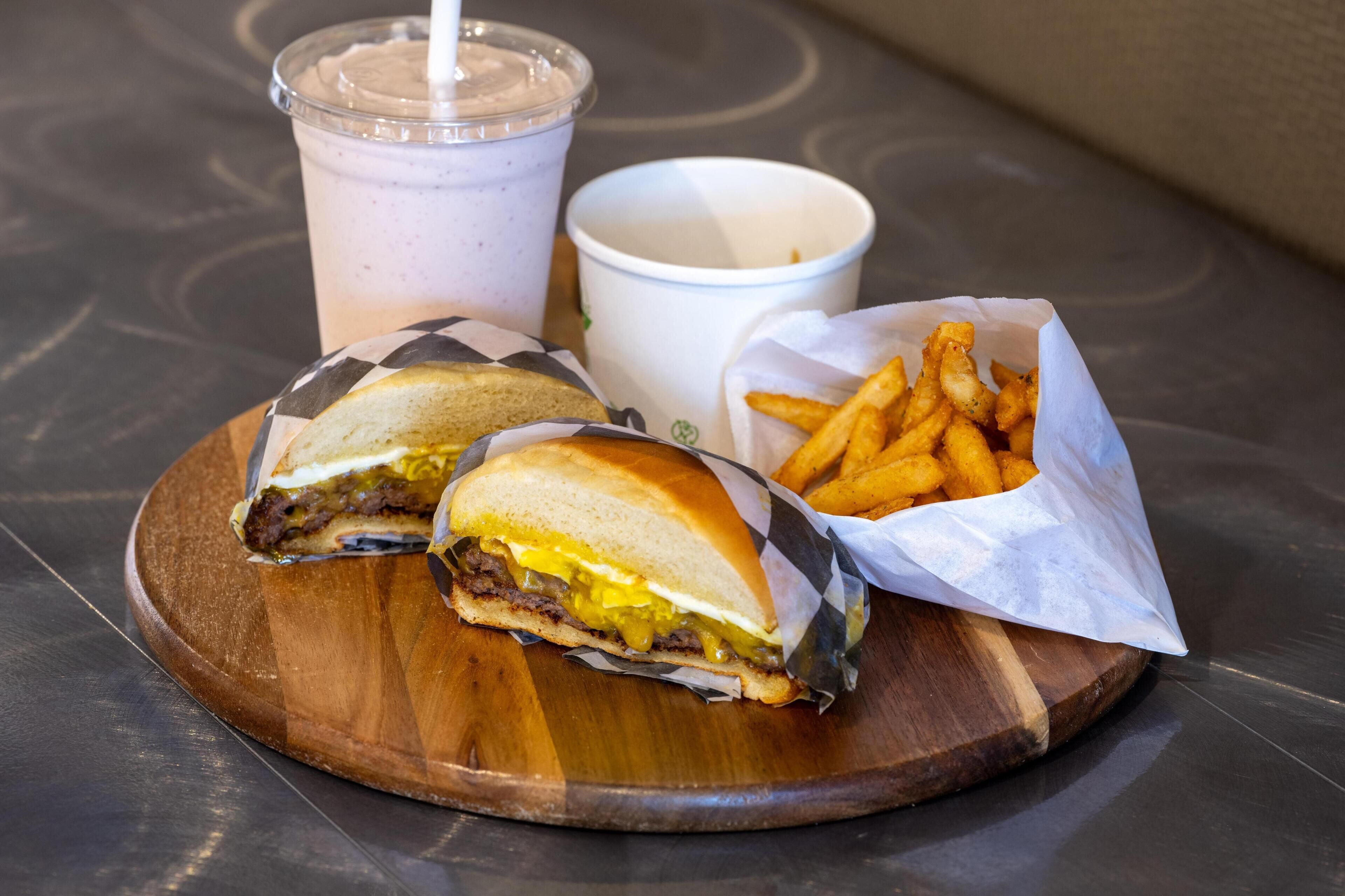 Una comida con un sándwich, papas fritas y una bebida sobre una tabla de madera.