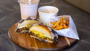 Una comida con un sándwich, papas fritas y una bebida sobre una tabla de madera.