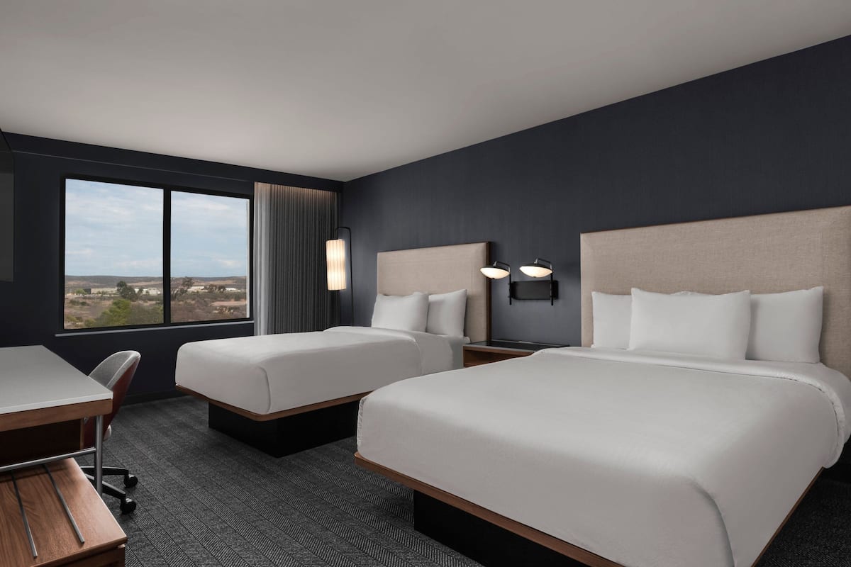 Une chambre d’hôtel avec deux lits, un bureau et une grande fenêtre donnant sur le paysage.
