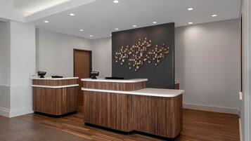 A reception area with two wooden reception desks, a modern abstract wall art, and recessed ceiling lighting.