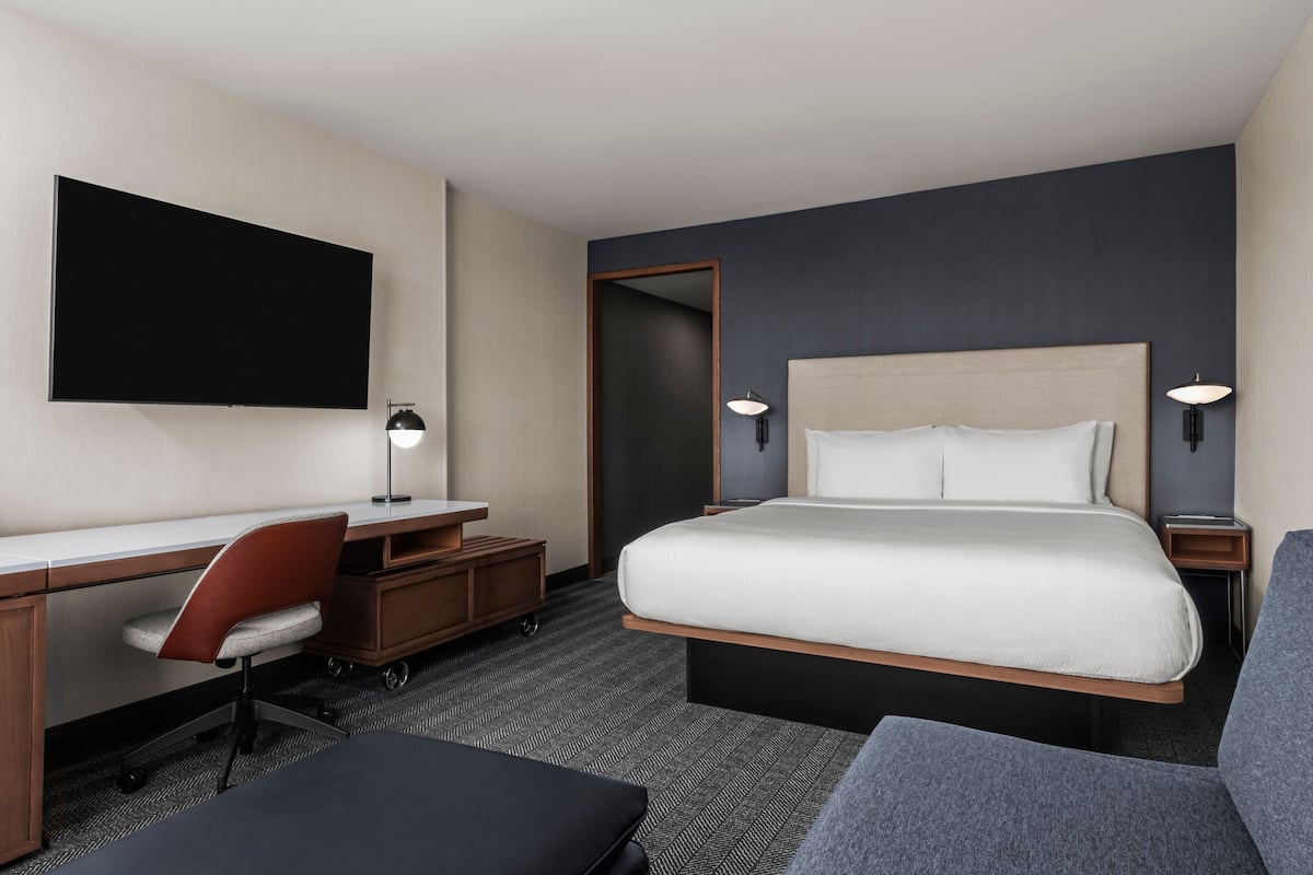 Une chambre d’hôtel avec un grand lit, un bureau, une chaise, une télévision et une lampe.