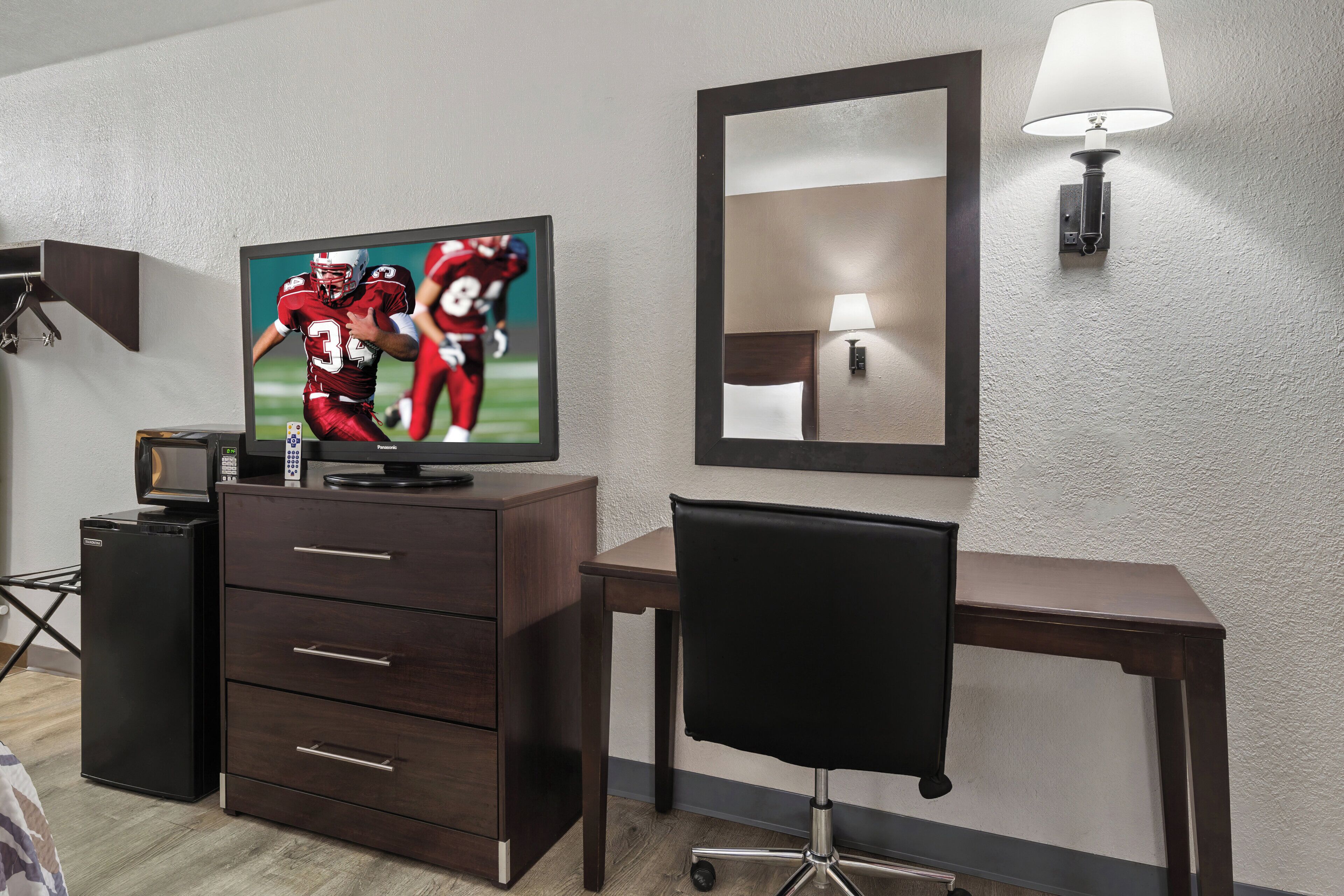 Una habitación de hotel con televisión, escritorio, silla, cómoda, lámpara y espejo.