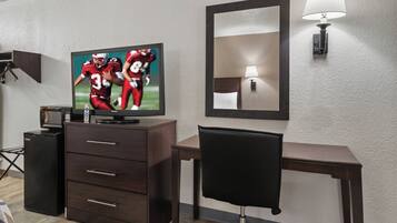A hotel room with a television, a desk, a chair, a dresser, a lamp, and a mirror.