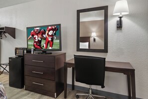 Une chambre d’hôtel équipée d’une télévision, d’un bureau, d’une chaise, d’une commode, d’une lampe et d’un miroir.