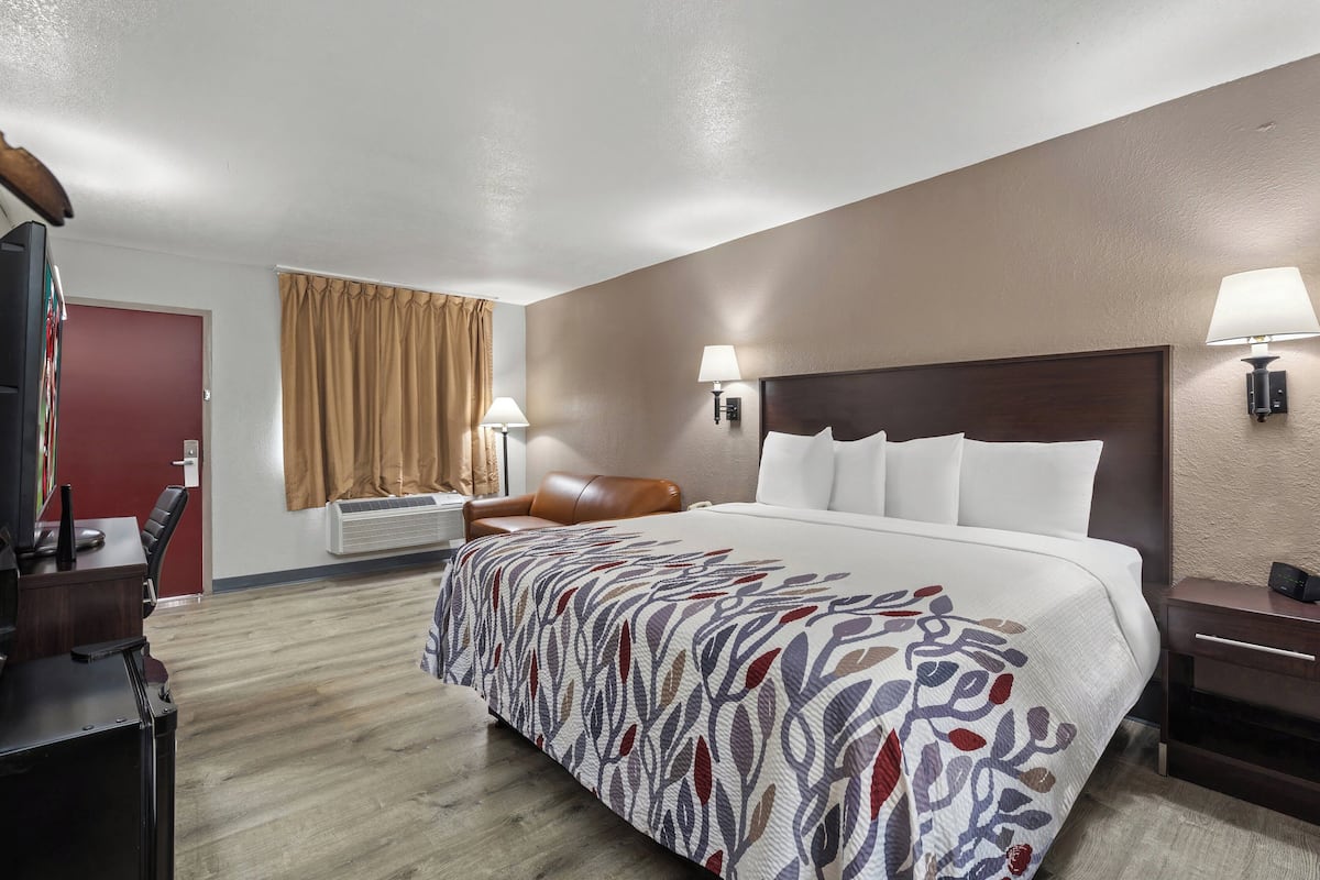 Ein Hotelzimmer mit einem großen Bett, einem Schreibtisch mit Computer, einem Sessel und einem Fernseher.