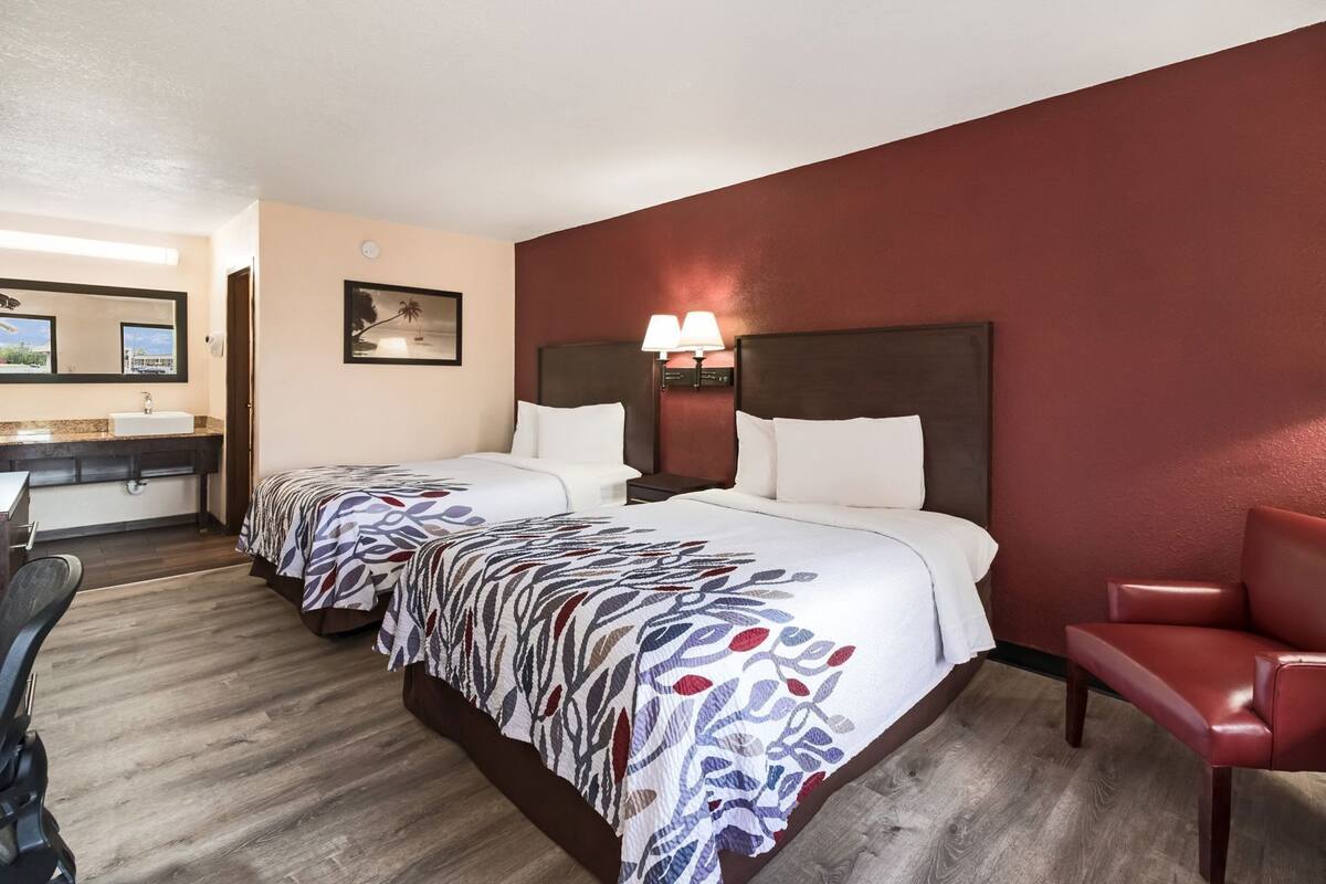 Ein Hotelzimmer mit zwei Betten, einem Schreibtisch, einem Stuhl und einem Badezimmer.