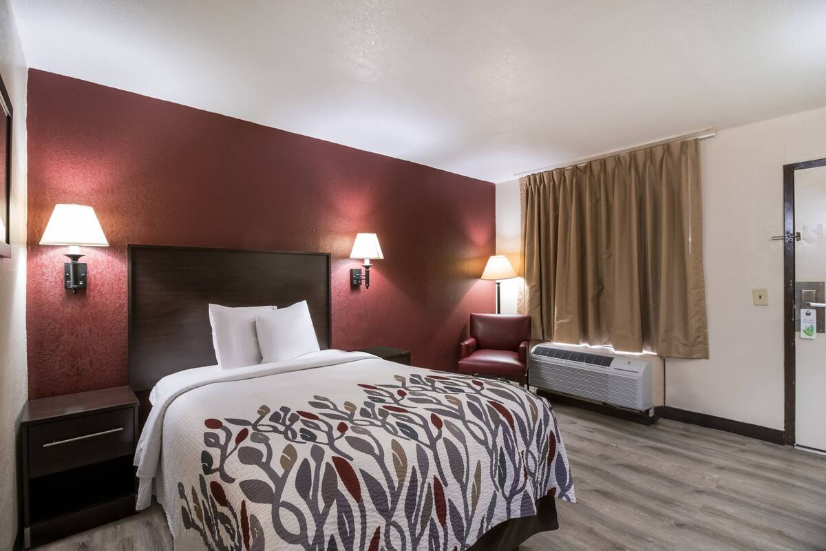 Ein Hotelzimmer mit einem Bett, zwei Nachttischlampen, einem Sessel, einer Klimaanlage und einer Tür.