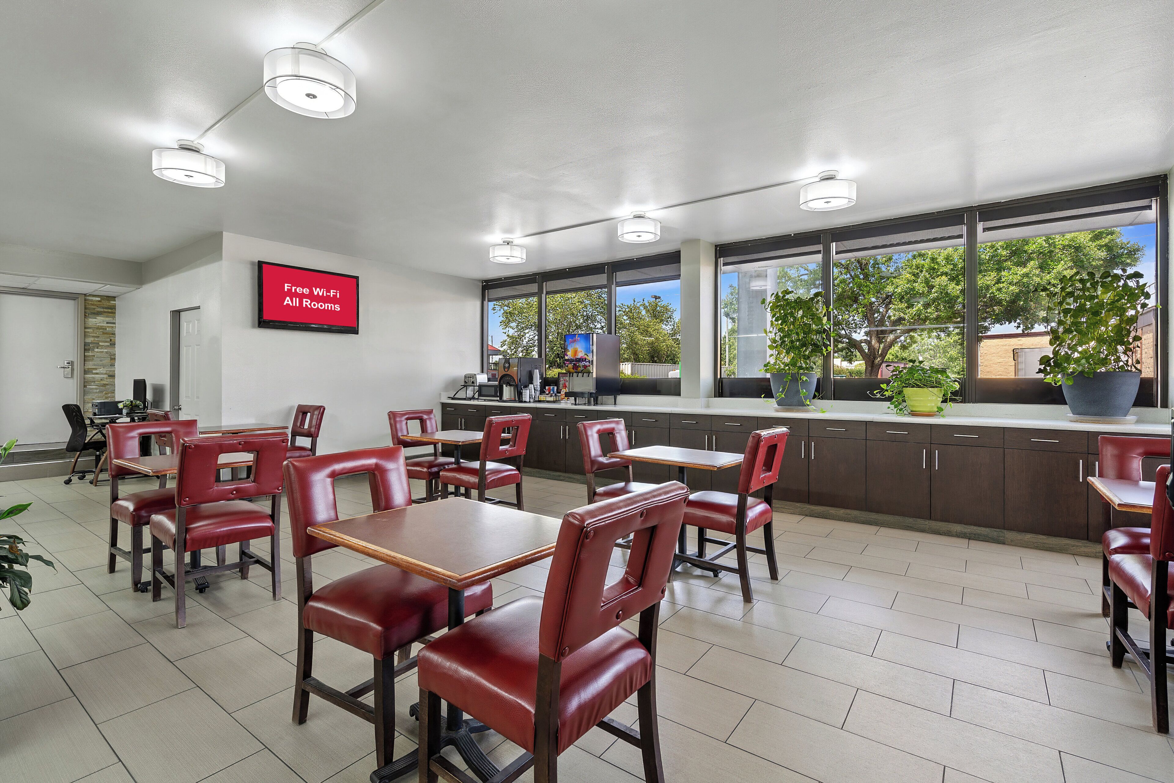 A restaurant with red leather chairs and tables, a kitchen area, and a sign indicating free Wi-Fi in all rooms.