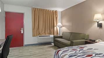 Une chambre d’hôtel avec un lit, une chaise, un bureau, une porte rouge, un climatiseur, une lampe et un téléphone.