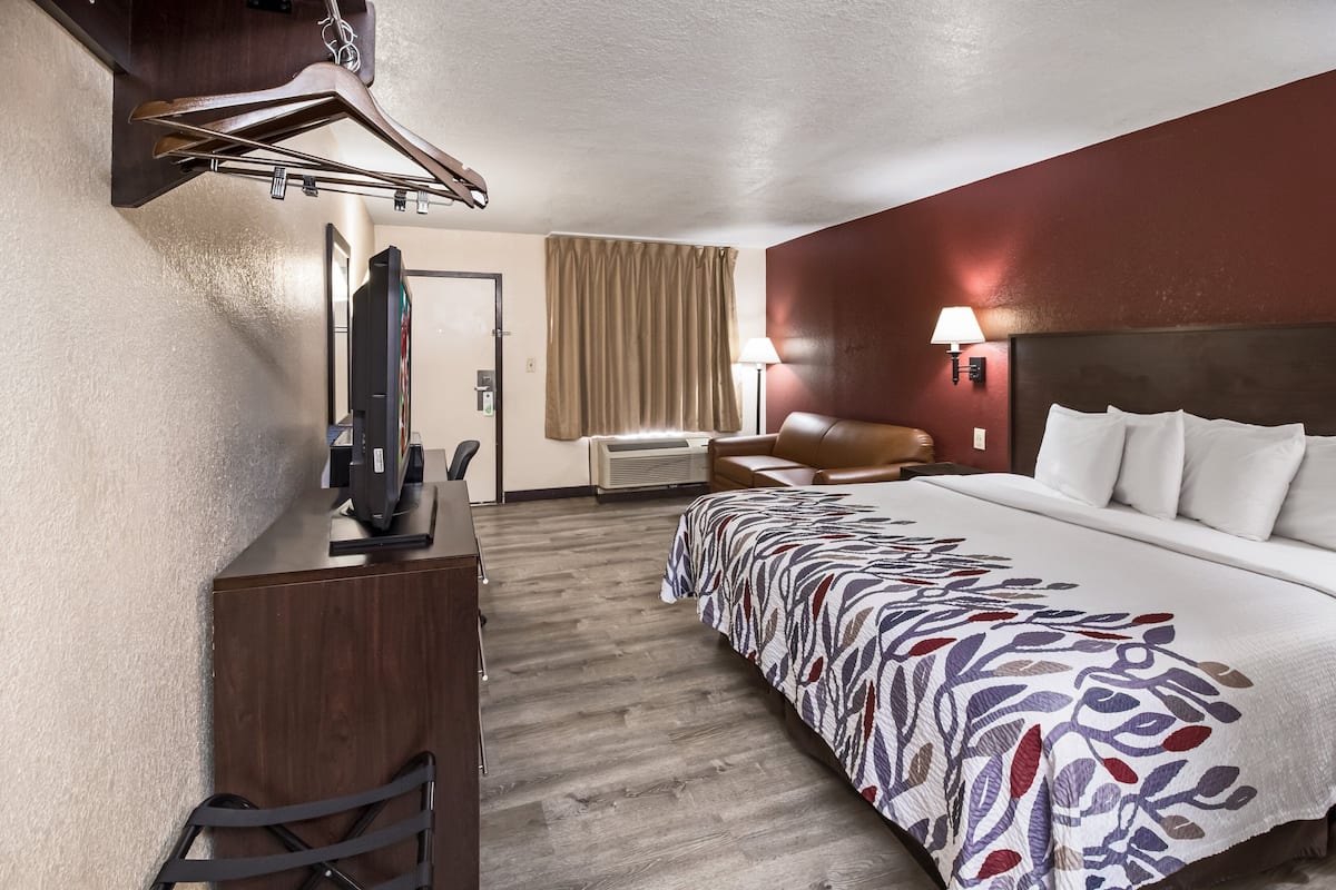 Ein Hotelzimmer mit einem Bett, einem Schreibtisch mit Fernseher, einem Sessel, einer Lampe und einem Kleiderhaken.