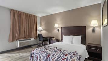 A hotel room with a bed, desk, chair, bedside lamps, and a window with curtains.