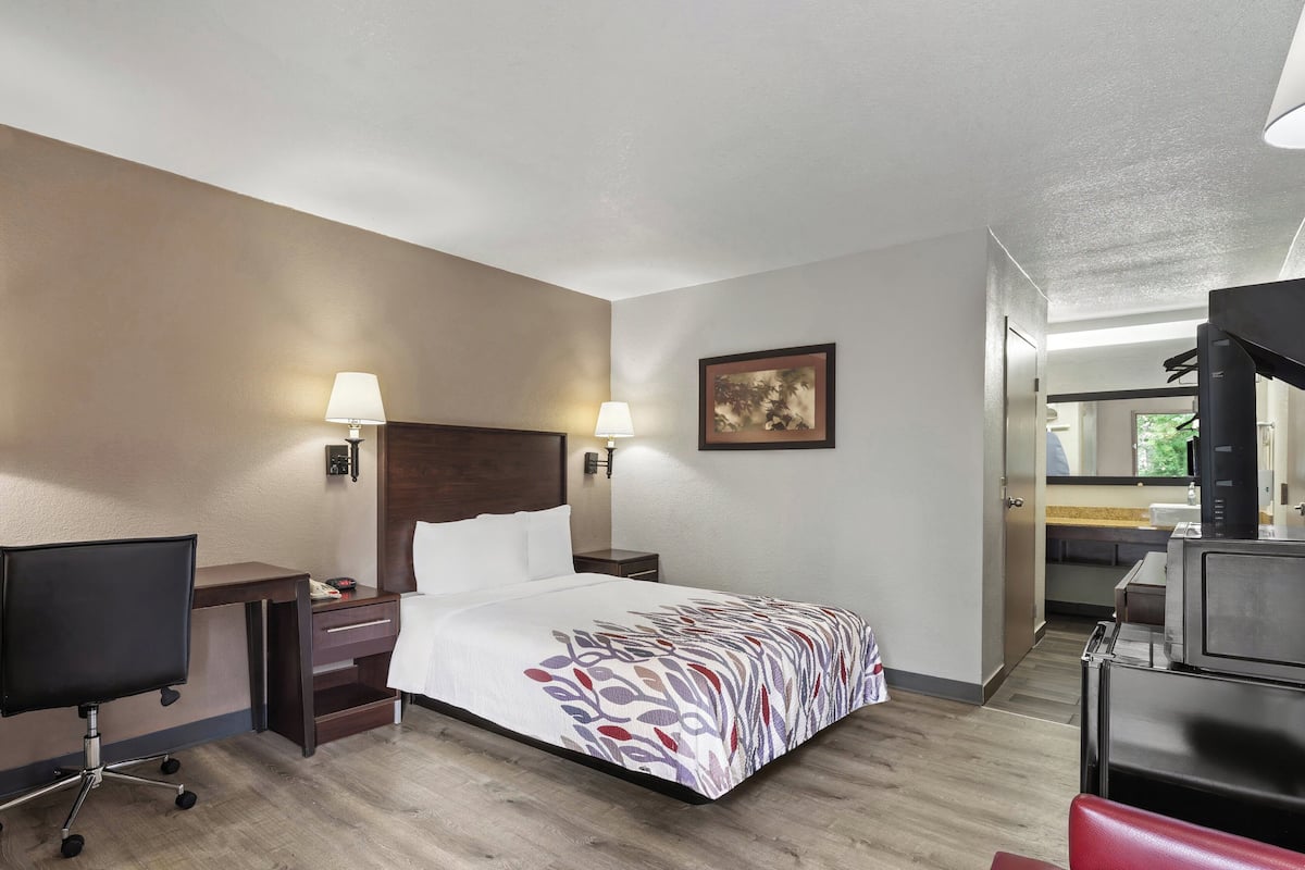 Ein Hotelzimmer mit Bett, Schreibtisch, Stuhl, Nachttisch und einem Bild an der Wand.