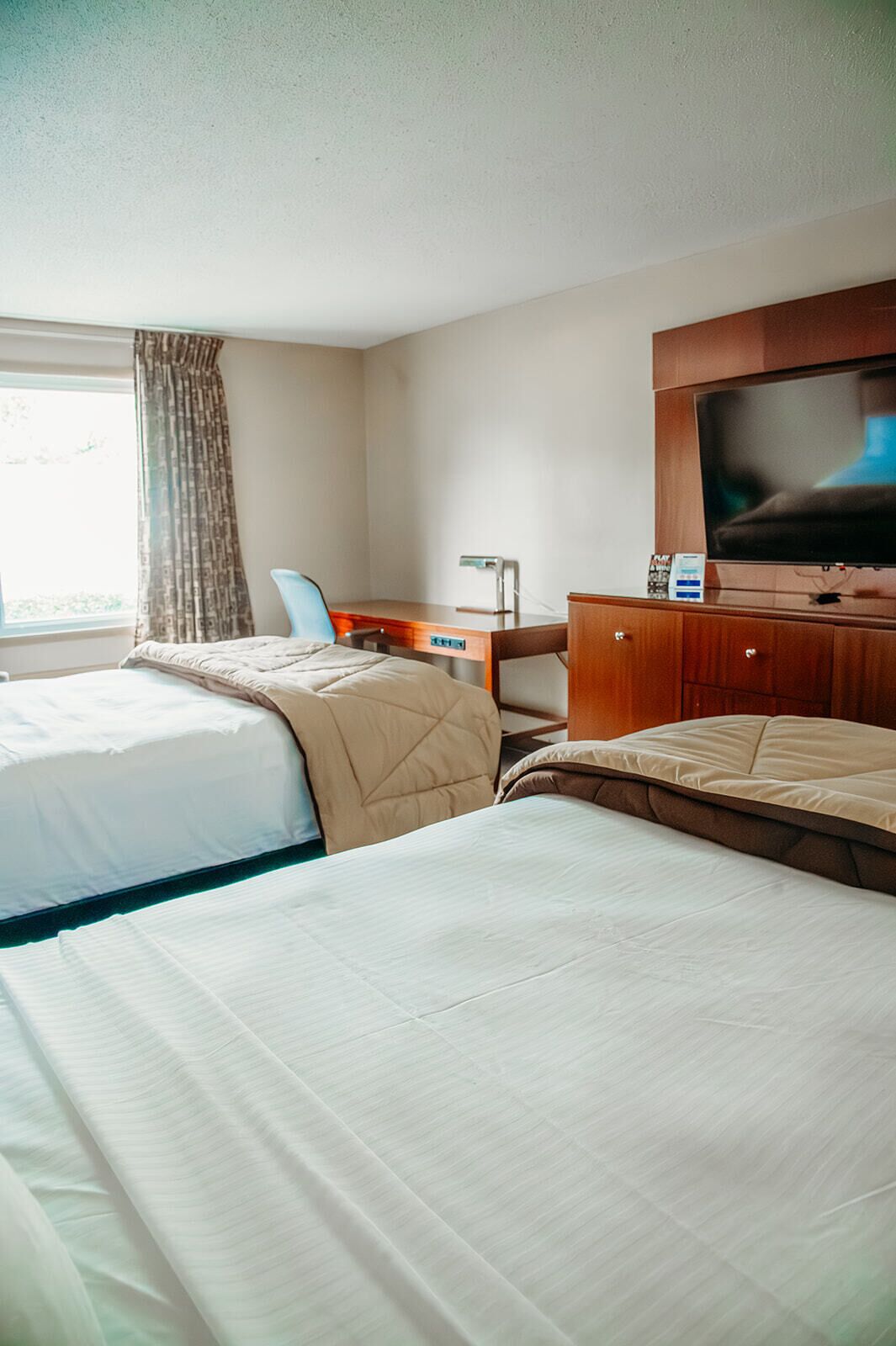 Een hotelkamer met twee bedden, een bureau met stoel, een televisie en een raam met gordijnen.