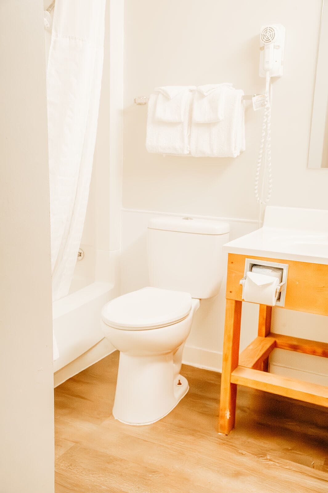 Et badeværelse med toilet, trækommode, håndklæderække og hårtørrer.