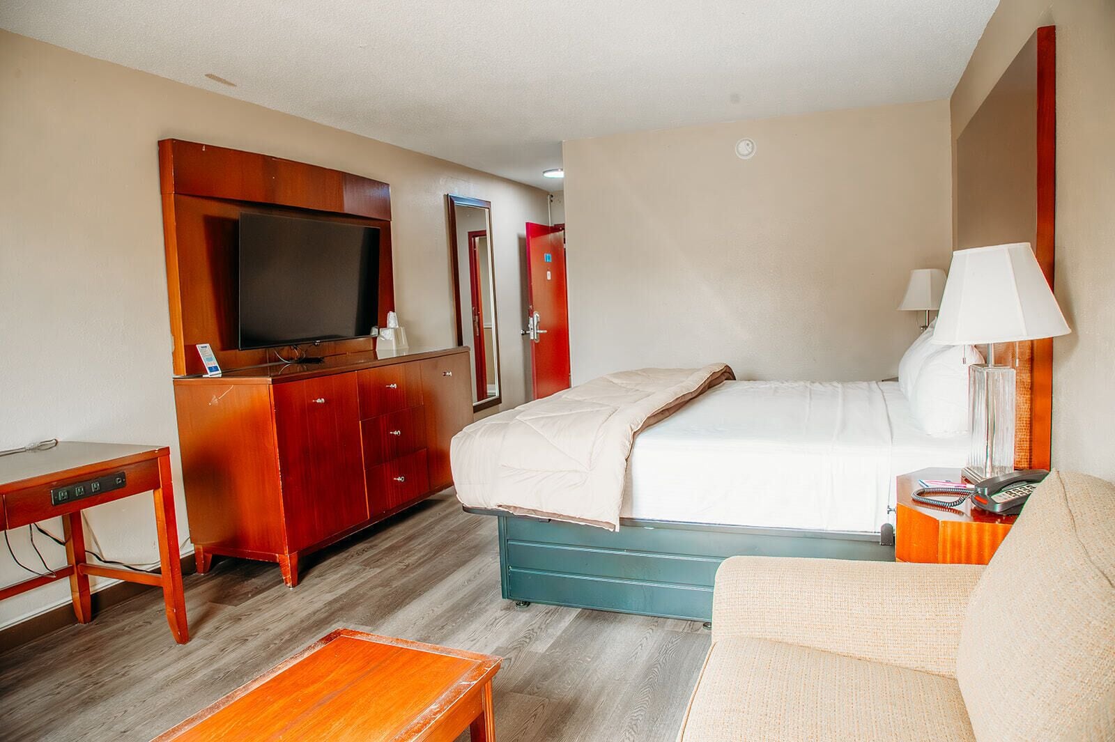 A hotel room with a bed, a desk, a TV, and a mirror.