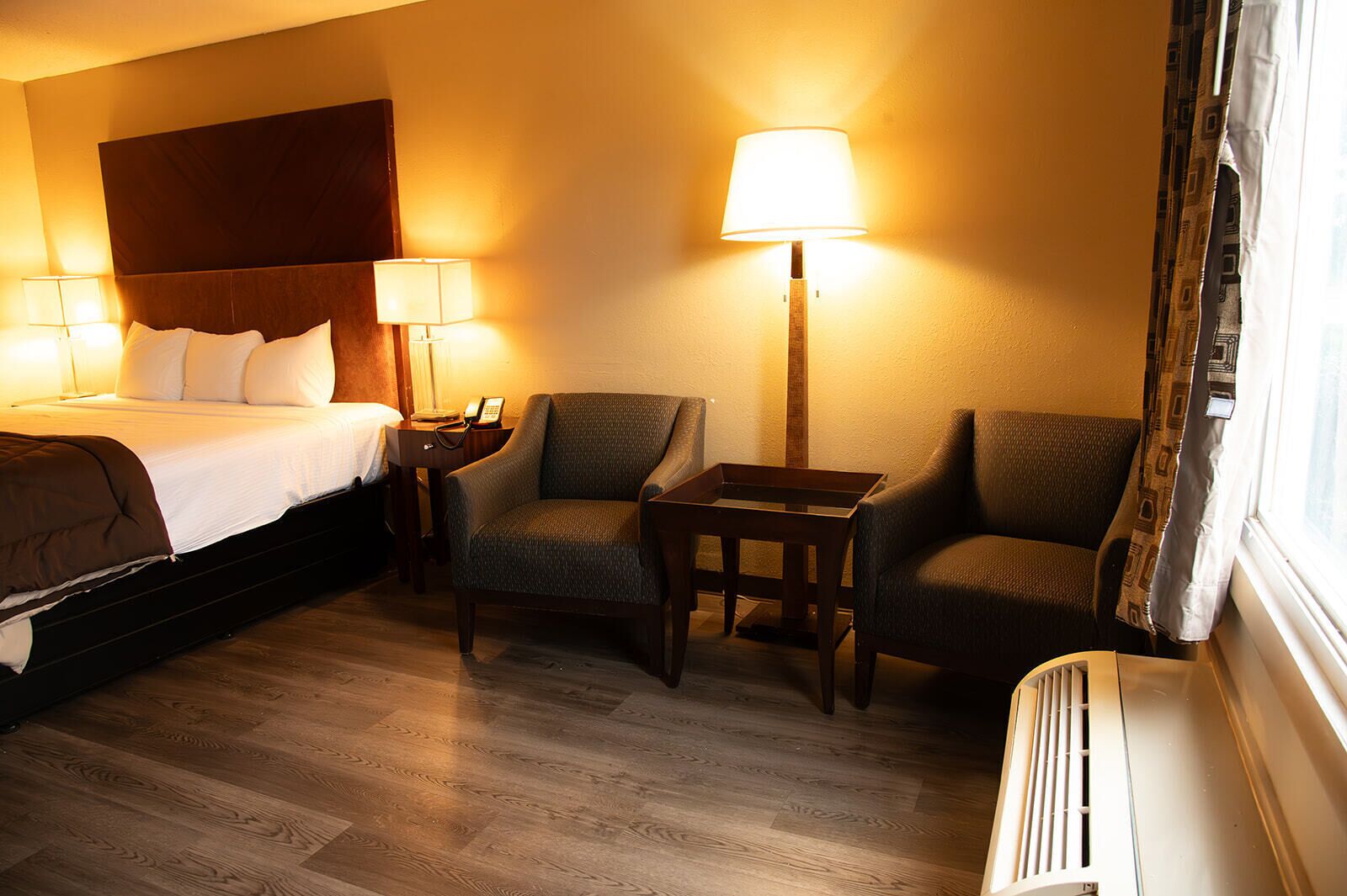 Ein Hotelzimmer mit einem Bett, zwei Sesseln, einem kleinen Tisch und einer Stehlampe.