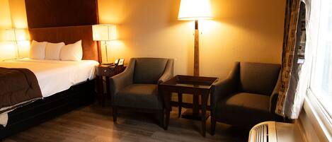 Ein Hotelzimmer mit einem Bett, zwei Sesseln, einem kleinen Tisch und einer Stehlampe.
