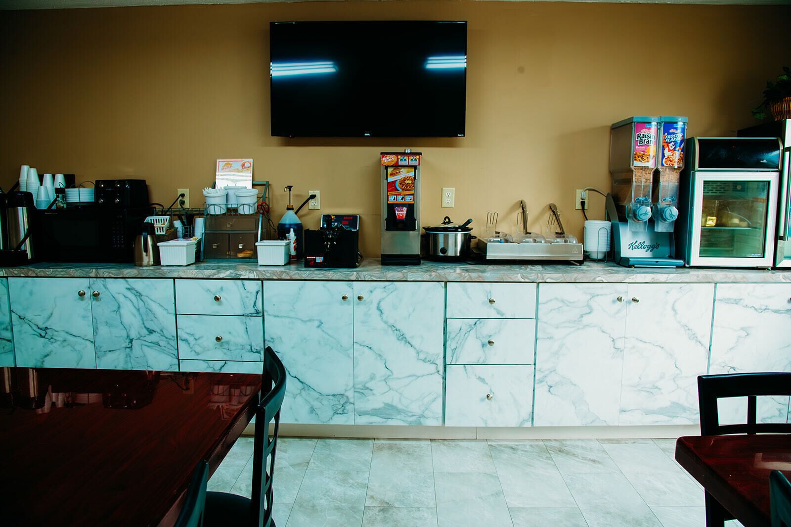 A kitchen with marble cabinets, a coffee machine, and a television mounted on the wall.