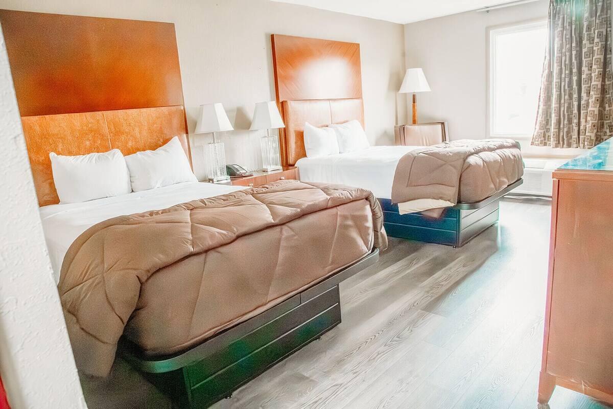 A hotel room with two beds, a desk, a chair, and a window with curtains.